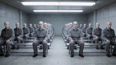Rows of identical seated figures in grey uniforms, receding to a vanishing point